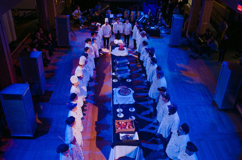 performance photo of dining hall employees standing around table full of prepared food
